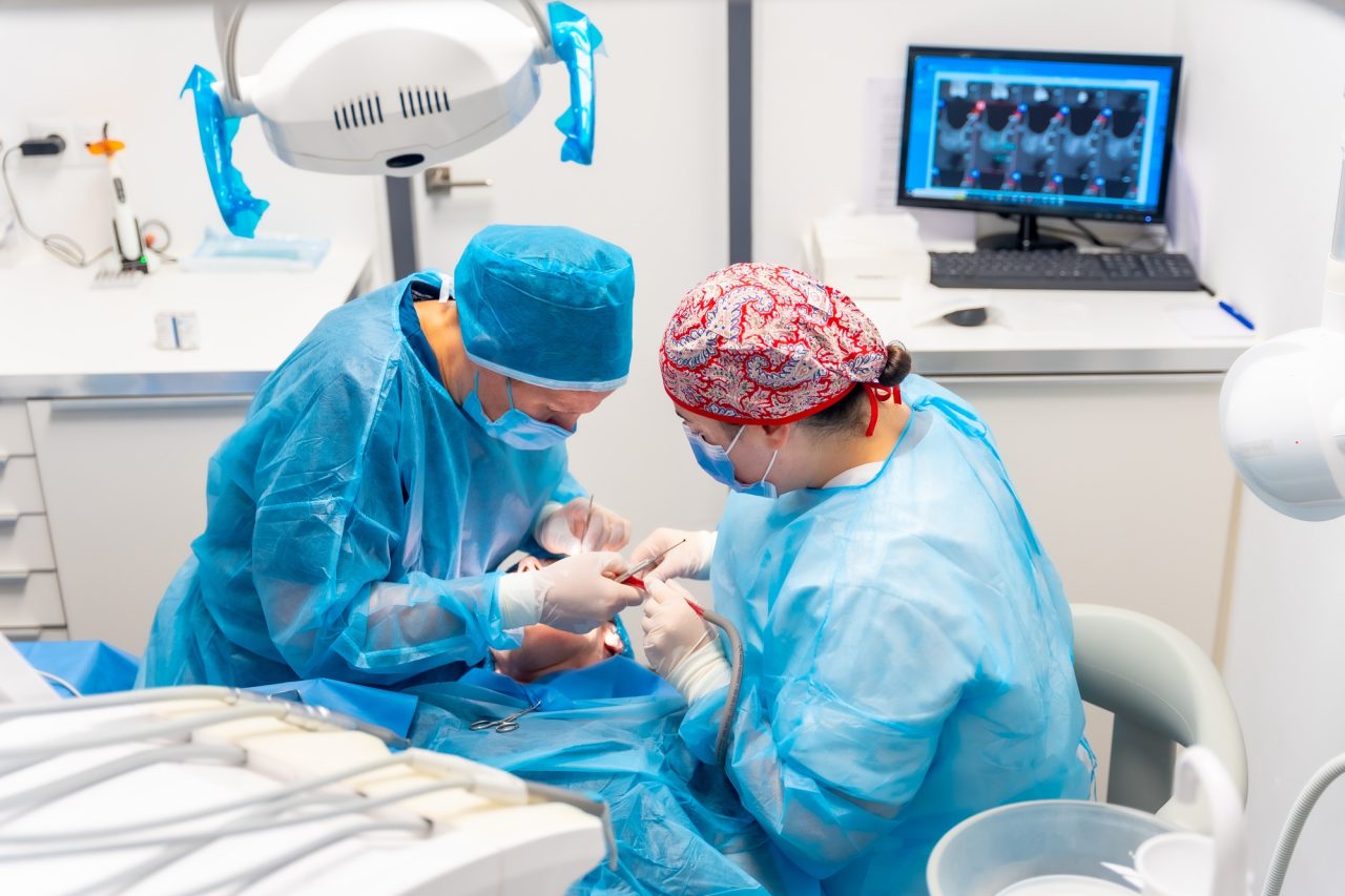 Female dentists in blue scrubs performing a complicated operation on a female patient sucking blood.jpg